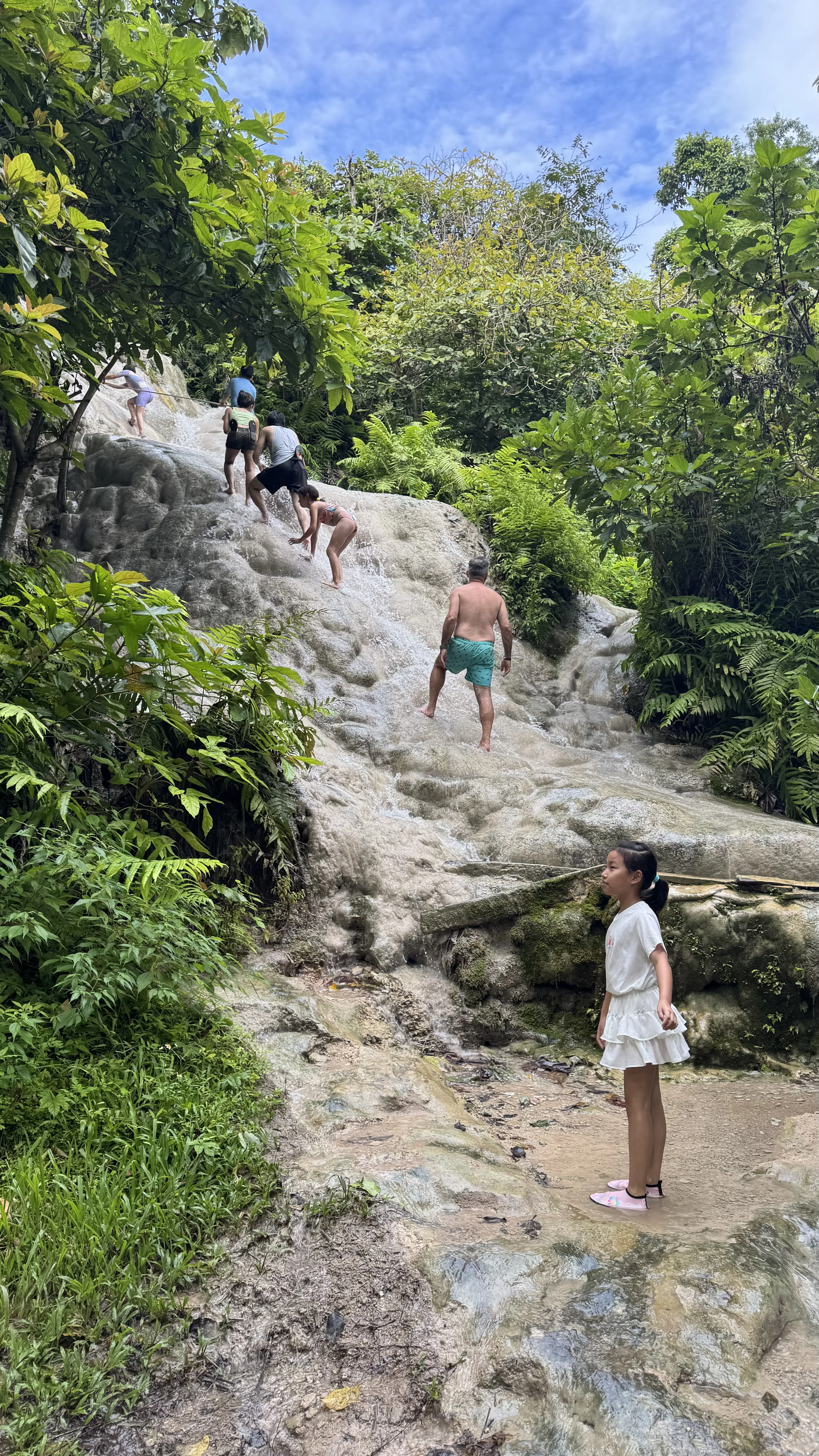 女儿站在粘粘瀑布的岩石旁，身后有人顺着水流攀爬