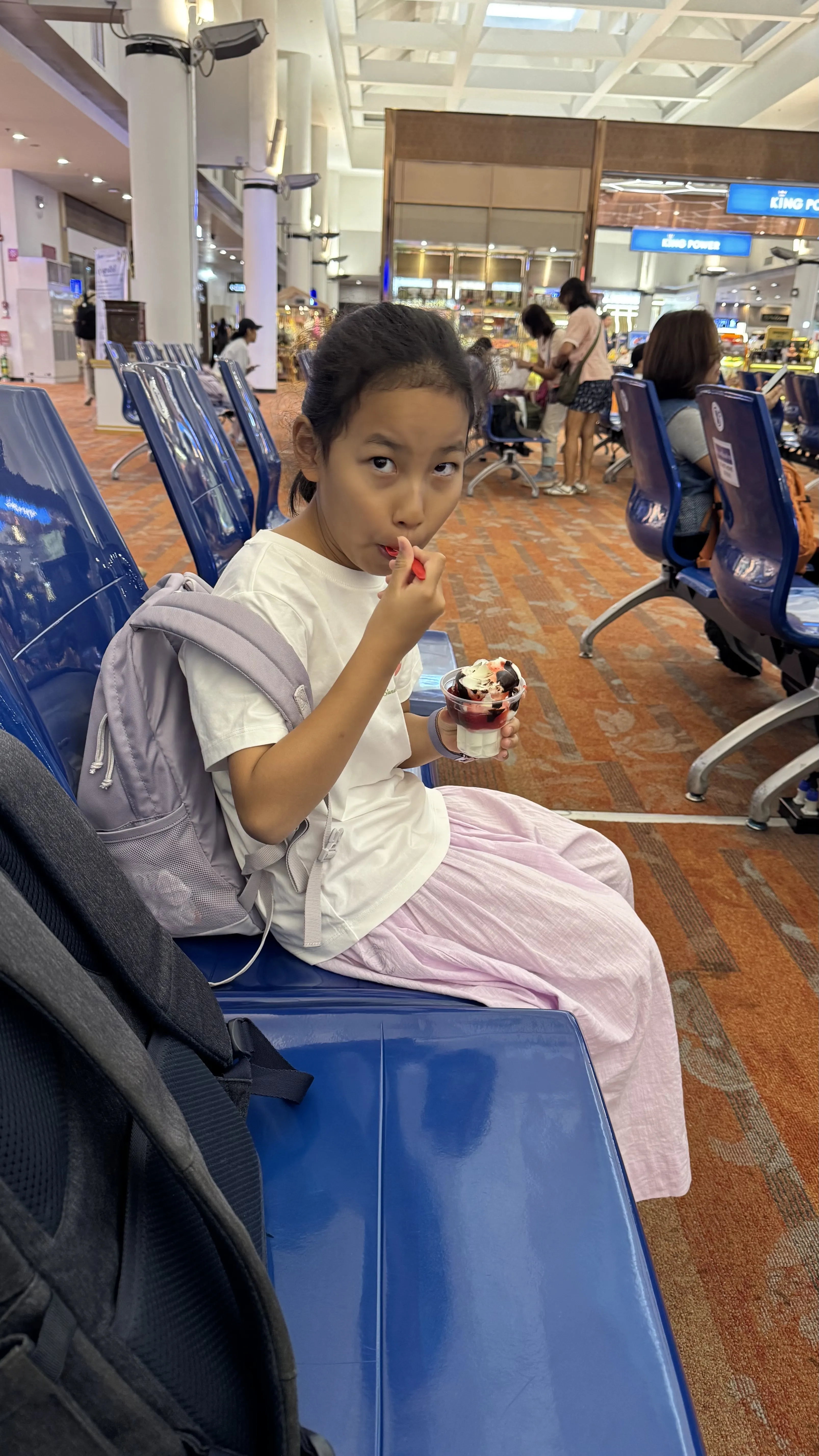 女儿坐在清迈机场的蓝色座椅上吃冰淇淋
